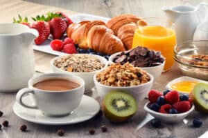 breakfast staples like a cup of coffee, cup of creamer, kiwi, berries, dry cereal, orange juice, croissants, and more